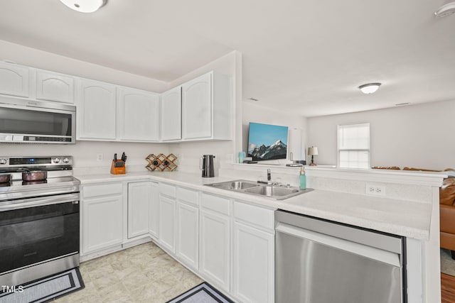 kitchen featuring appliances with stainless steel finishes, a peninsula, light countertops, white cabinetry, and a sink