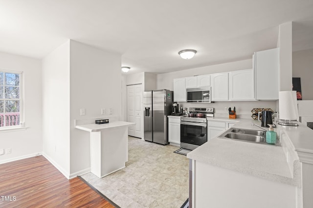 kitchen with baseboards, white cabinets, light wood-style flooring, stainless steel appliances, and light countertops