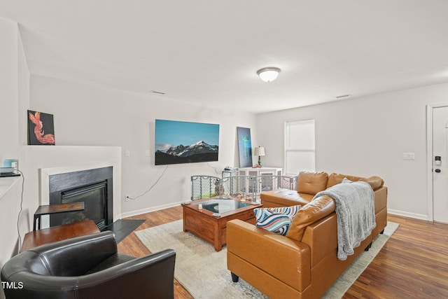 living area featuring a fireplace with flush hearth, baseboards, and wood finished floors