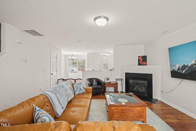 living area featuring a notable chandelier, visible vents, a glass covered fireplace, wood finished floors, and baseboards