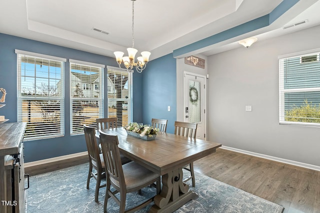 dining space with a tray ceiling, wood finished floors, visible vents, and baseboards