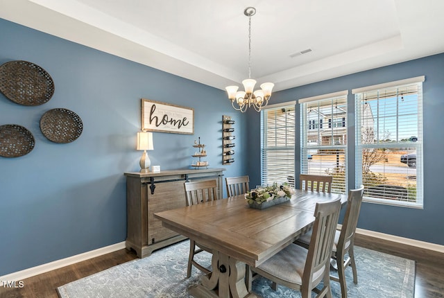 dining area with visible vents, baseboards, a tray ceiling, and wood finished floors