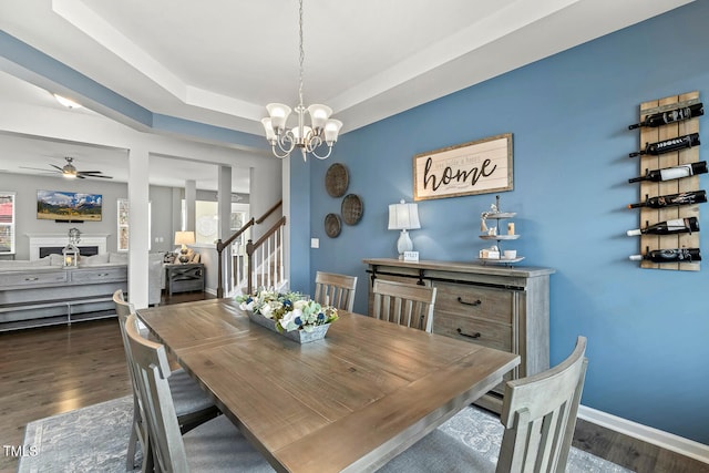 dining space with baseboards, stairs, a tray ceiling, and wood finished floors