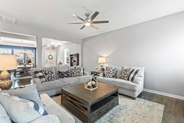 living room with visible vents, ceiling fan with notable chandelier, dark wood-type flooring, and baseboards