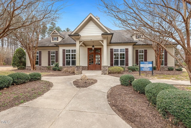 view of front of home featuring french doors, stone siding, and a shingled roof