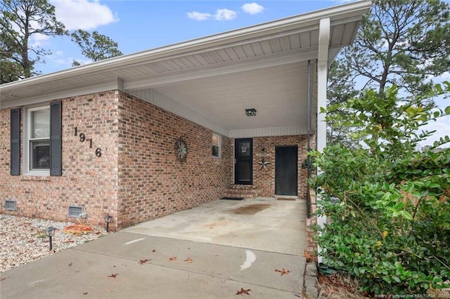 exterior space with a carport, brick siding, crawl space, and concrete driveway