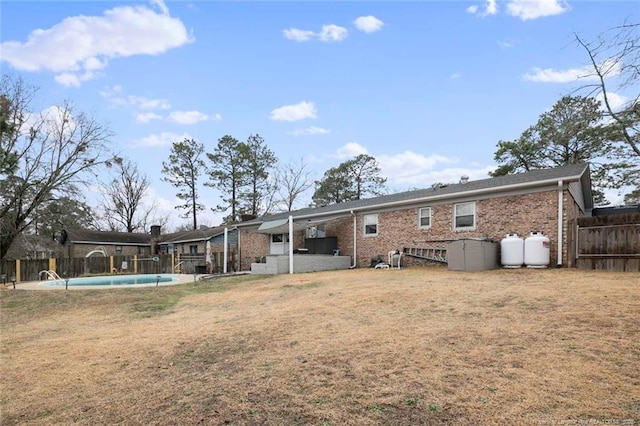 rear view of property with a fenced in pool, brick siding, fence, and a lawn