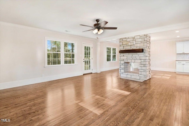 unfurnished living room with light wood-type flooring, crown molding, a stone fireplace, and baseboards