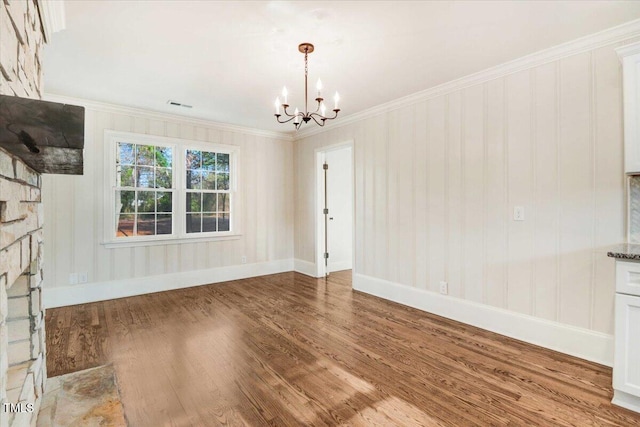 unfurnished dining area featuring crown molding, visible vents, an inviting chandelier, wood finished floors, and baseboards