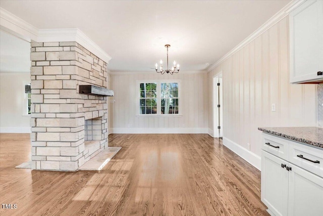 unfurnished living room featuring baseboards, crown molding, light wood-type flooring, a fireplace, and a notable chandelier