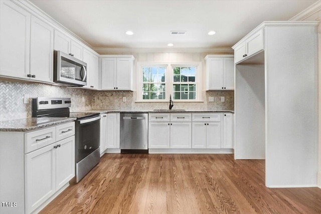 kitchen featuring light wood finished floors, light stone counters, stainless steel appliances, white cabinetry, and a sink