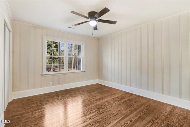 spare room featuring dark wood-style flooring, visible vents, crown molding, and baseboards