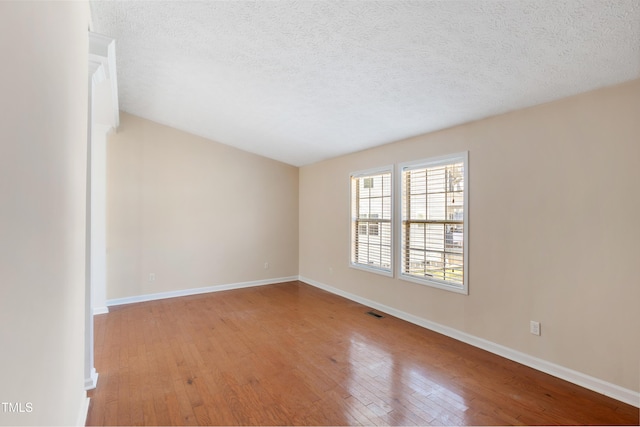 unfurnished room with visible vents, a textured ceiling, hardwood / wood-style flooring, and baseboards