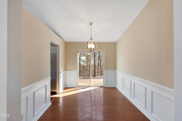 unfurnished dining area with wainscoting, a decorative wall, and wood finished floors