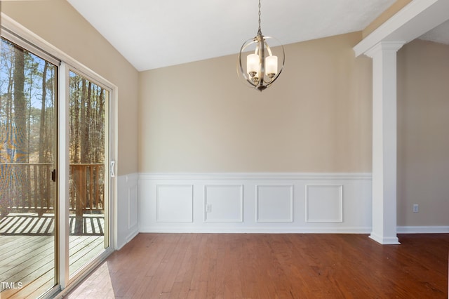 unfurnished dining area with ornate columns, a notable chandelier, wood finished floors, and a wainscoted wall