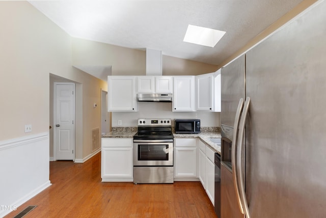 kitchen featuring visible vents, lofted ceiling with skylight, appliances with stainless steel finishes, light wood-type flooring, and under cabinet range hood