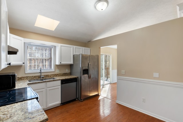 kitchen with appliances with stainless steel finishes, white cabinetry, a sink, vaulted ceiling with skylight, and under cabinet range hood