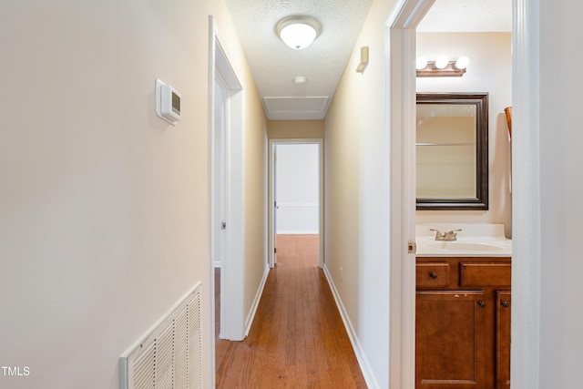 corridor featuring visible vents, a sink, a textured ceiling, light wood-type flooring, and baseboards