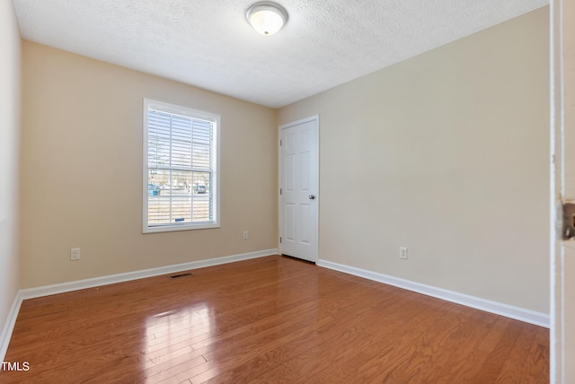 unfurnished room featuring a textured ceiling, wood finished floors, visible vents, and baseboards