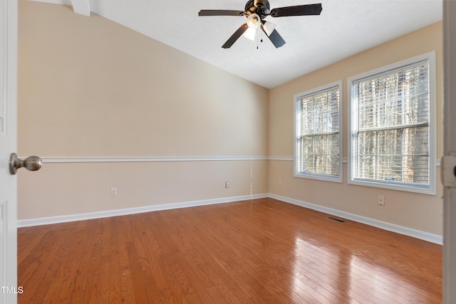 spare room with wood-type flooring, visible vents, a ceiling fan, vaulted ceiling, and baseboards