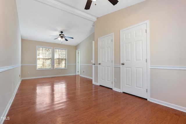 spare room featuring lofted ceiling with beams, wood finished floors, and baseboards