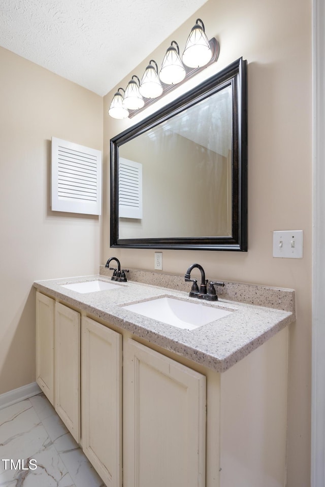 bathroom featuring double vanity, marble finish floor, a textured ceiling, and a sink