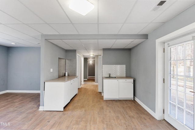 kitchen with light countertops, visible vents, white cabinets, light wood-type flooring, and baseboards