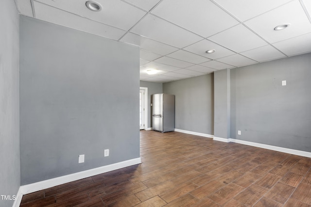 unfurnished room with baseboards, a drop ceiling, and wood finished floors