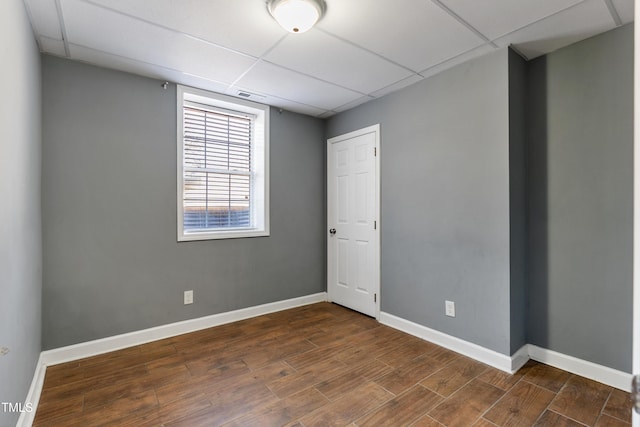 spare room with dark wood-type flooring, a paneled ceiling, and baseboards