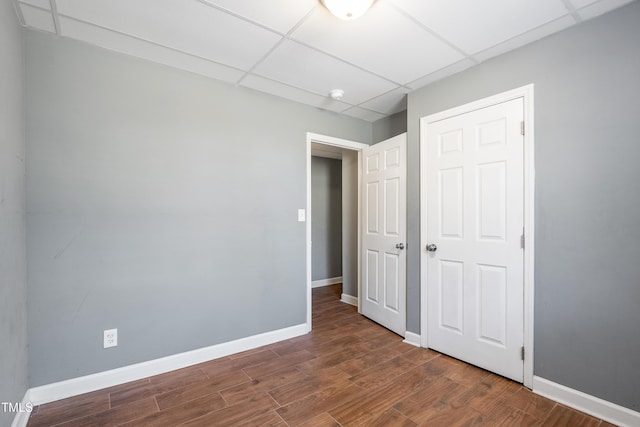 unfurnished bedroom with dark wood-type flooring, a paneled ceiling, and baseboards