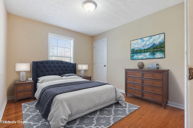 bedroom featuring a textured ceiling, baseboards, and wood finished floors