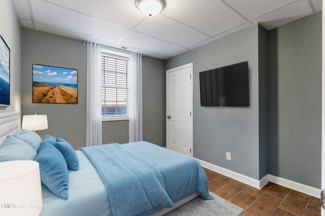 bedroom featuring a paneled ceiling, dark wood-style floors, and baseboards