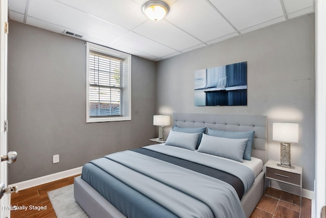 bedroom with a drop ceiling, wood finished floors, visible vents, and baseboards