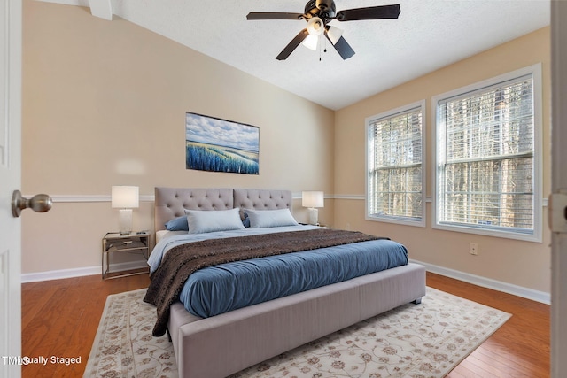 bedroom featuring a ceiling fan, vaulted ceiling, a textured ceiling, wood finished floors, and baseboards