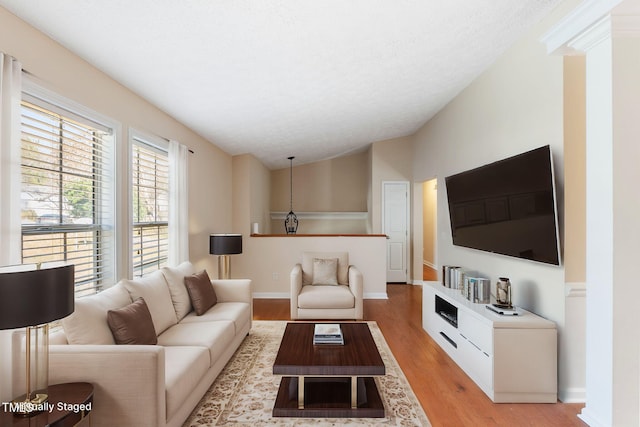 living area with lofted ceiling, light wood finished floors, baseboards, and a textured ceiling