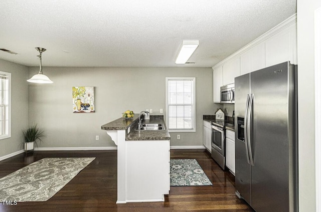 kitchen featuring dark countertops, appliances with stainless steel finishes, a peninsula, white cabinetry, and a sink