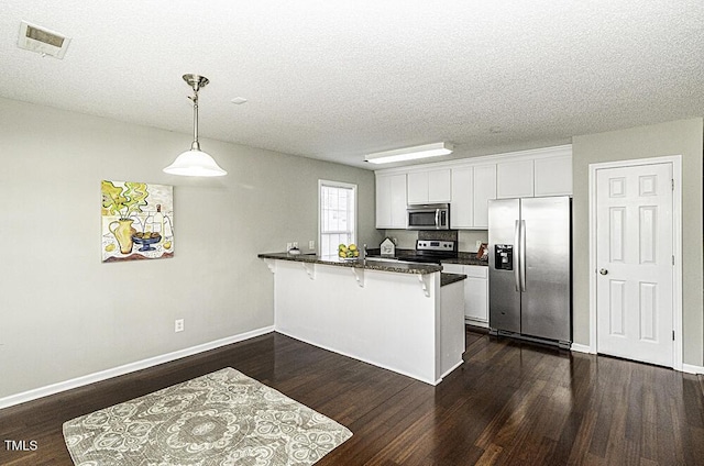 kitchen featuring visible vents, appliances with stainless steel finishes, a peninsula, a kitchen bar, and white cabinetry