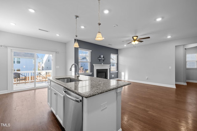 kitchen featuring visible vents, an island with sink, a sink, stainless steel dishwasher, and a glass covered fireplace