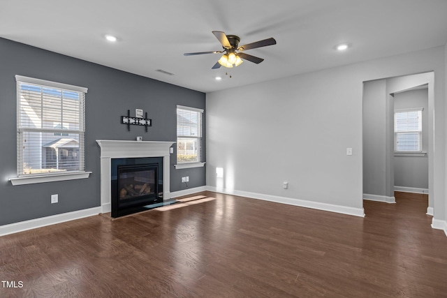 unfurnished living room featuring a glass covered fireplace, plenty of natural light, baseboards, and wood finished floors