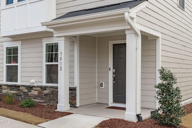 property entrance with a porch, stone siding, and a shingled roof