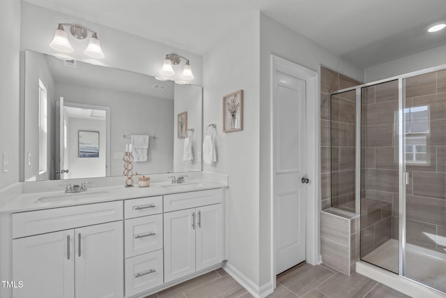 full bath featuring double vanity, a stall shower, baseboards, and a sink