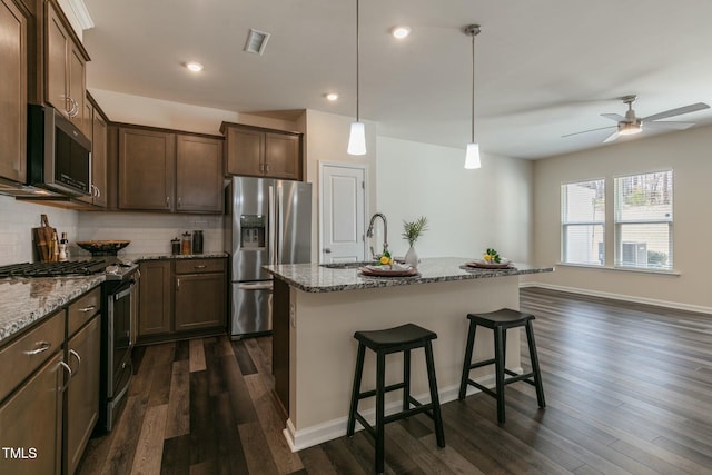 kitchen with visible vents, appliances with stainless steel finishes, a sink, stone counters, and backsplash