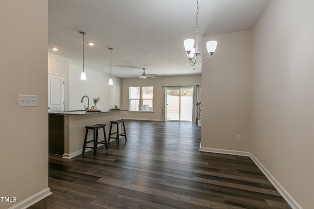 kitchen featuring baseboards, dark wood finished floors, open floor plan, a kitchen bar, and ceiling fan with notable chandelier