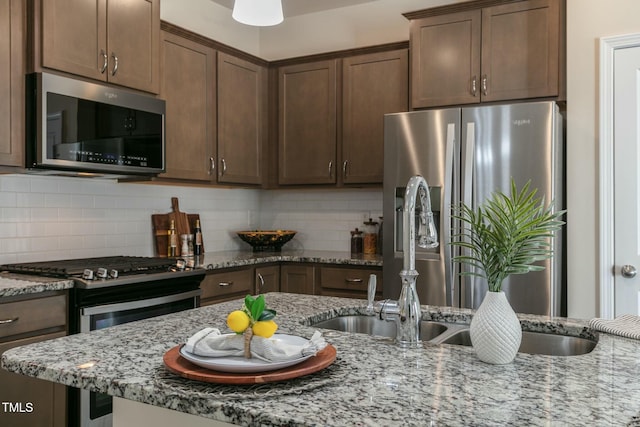 kitchen with light stone counters, decorative backsplash, appliances with stainless steel finishes, dark brown cabinetry, and a sink