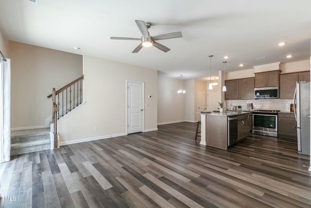 kitchen with a kitchen island with sink, open floor plan, appliances with stainless steel finishes, backsplash, and dark wood-style floors