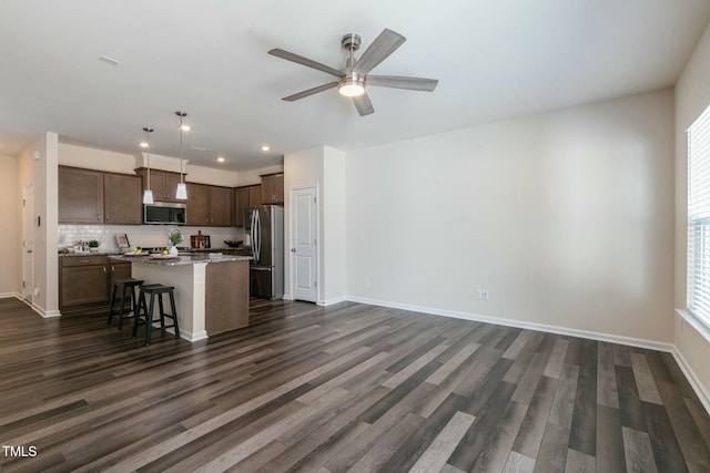 kitchen with dark brown cabinetry, dark wood-type flooring, baseboards, appliances with stainless steel finishes, and a center island