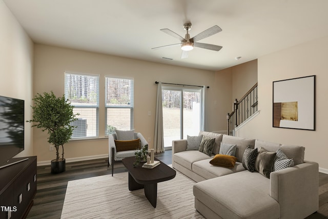 living area with ceiling fan, visible vents, baseboards, stairs, and dark wood-style floors