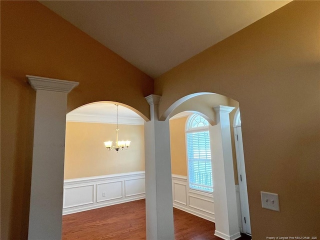 room details with a wainscoted wall, a decorative wall, an inviting chandelier, wood finished floors, and ornate columns