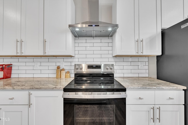 kitchen with stainless steel electric stove, tasteful backsplash, freestanding refrigerator, white cabinets, and extractor fan