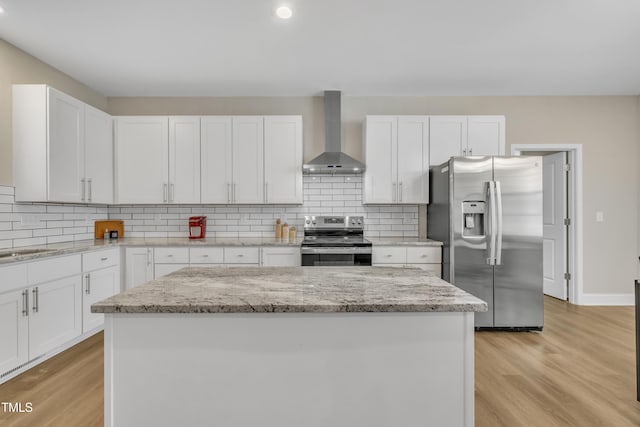 kitchen with wall chimney range hood, tasteful backsplash, appliances with stainless steel finishes, and light wood finished floors